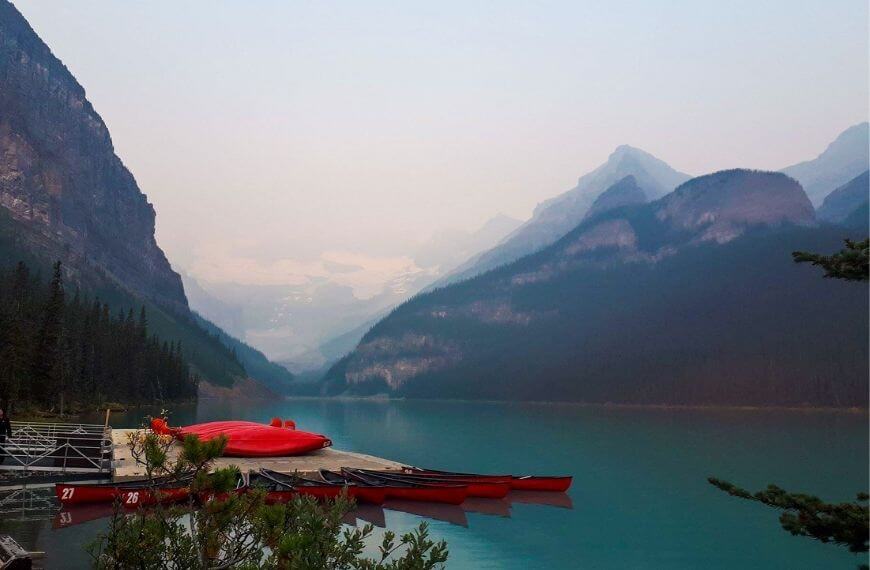 Lake louise with smoke and mountains in the background and the famous red canoes on the water