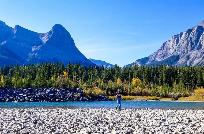 girl by river edge in front of mountains
