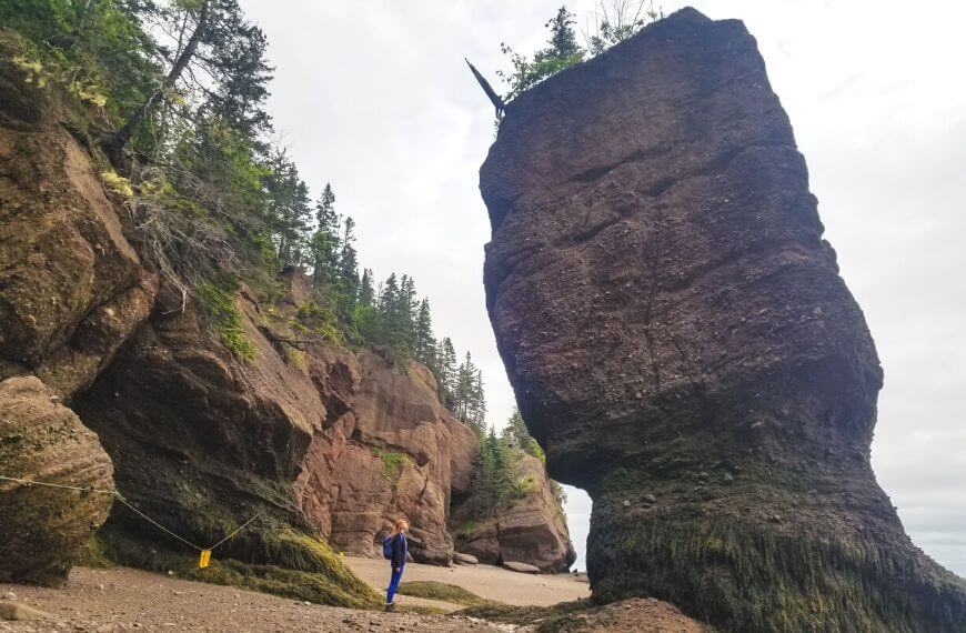 me standing under a towering rock formation created by the bay of fundy high tides before kayaking at hopewell rocks