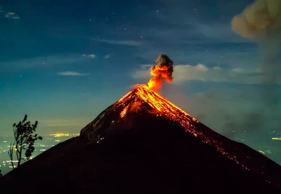 The top of a volcano with bright red lava flowing down the side during the night - a view from the top of one of the best volcano hikes in guatemala