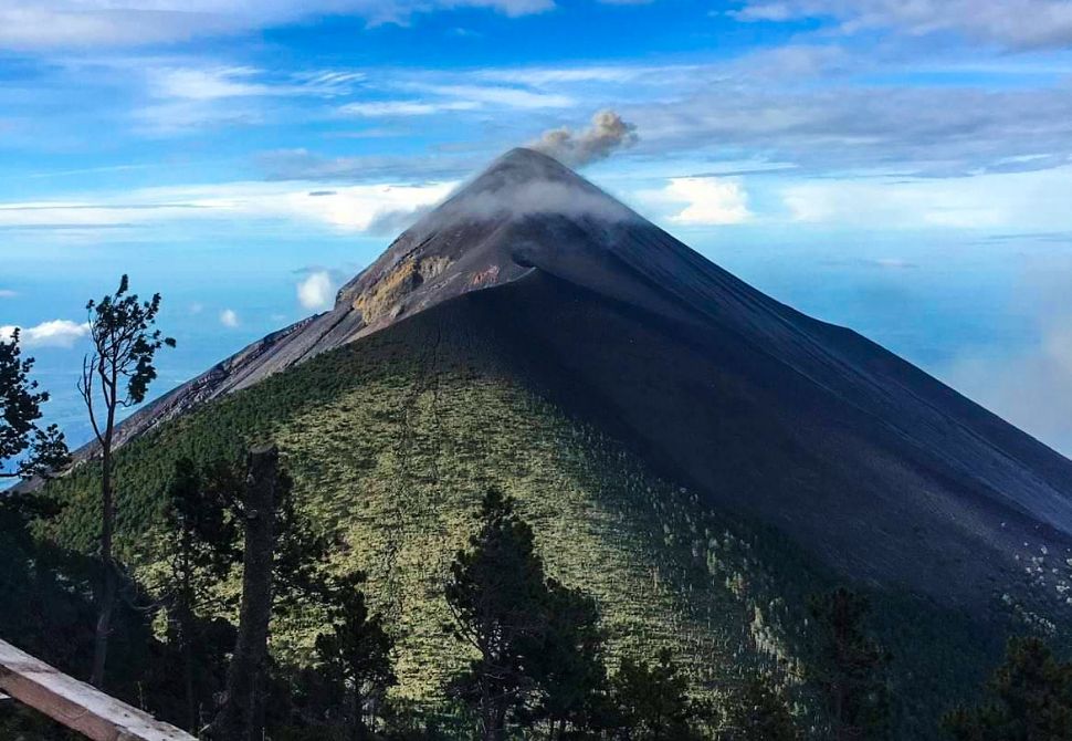 a daytime shot of the top of fuego volcano with a plume of smoke coming out of the top.