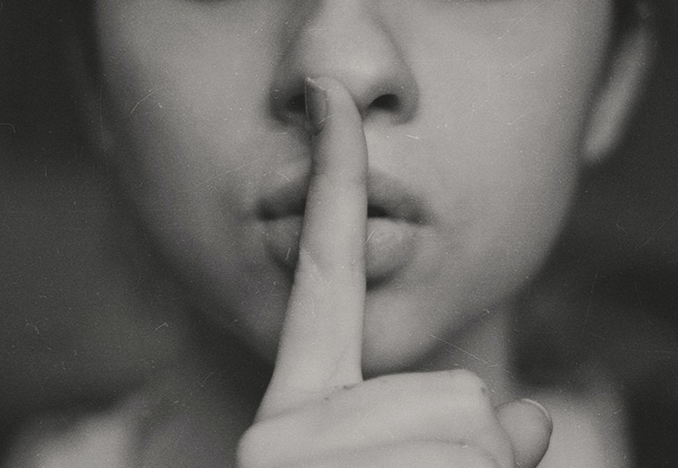 a black and white image of a girl holding her index finger up to ther lips to show being quiet